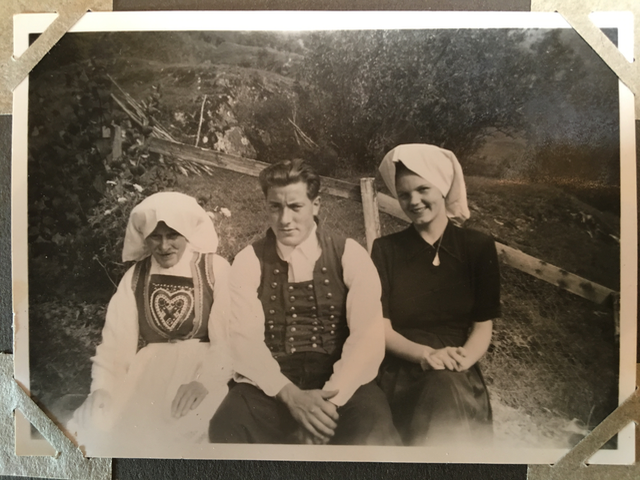 Bilde av tre personer. I midten mann kledd i bunad, til venstre person med kvithue og kvinnebunad, til høyre kvinne i kjole og kvithue.